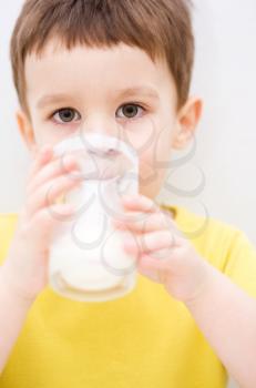 Cute little boy is dipping his tongue in the glass of milk