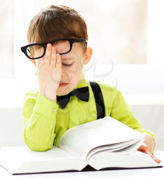 Cute little boy is reading book while sitting at table, indoor shoot