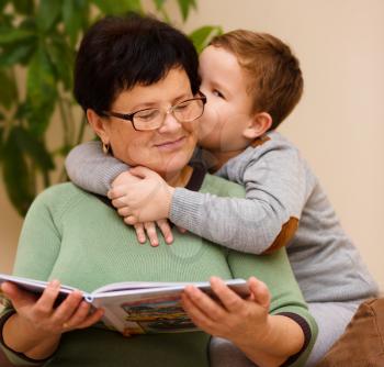 Grandmother is reading book with her grandson, indoor