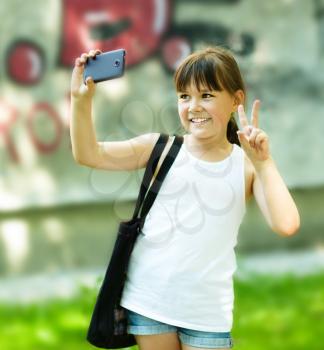 Cute happy girl makes self-portrait on the smartphone