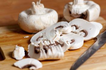 Whole and sliced white mushrooms in kitchen on wooden Board