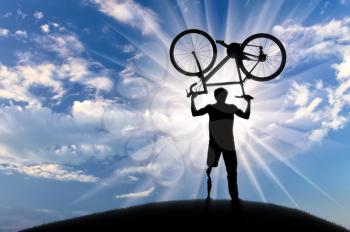 Disabled with prosthetic leg standing on hill and holding bicycle over his head day. Concept disabled and sport
