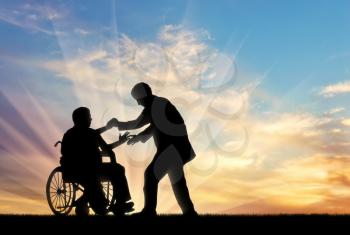 Man helps man in wheelchair to stand up on background sunset. Concept help disabled persons