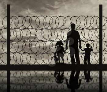Silhouette of a family with children of refugees and fence with barbed wire on the background of the beautiful sky and reflection