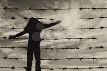 Concept of refugee. Silhouette of a refugee child near the fence of barbed wire