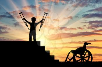 Happy disabled boy standing on sters with crutches in his hands and wheelchair sunset. Concept happy disabled