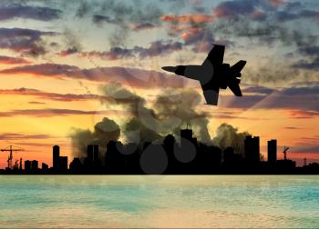 Silhouette of the city in a smoke on a background of a beautiful sunset and sea combat fighter