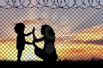 Concept of refugee. Silhouette of mother and child refugees at the border fence at sunset