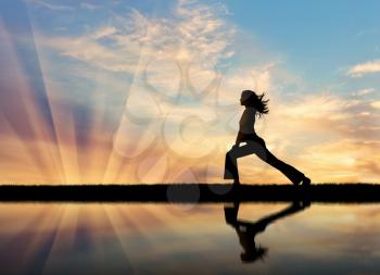 Concept of meditation and relaxation. Silhouette of a girl practicing yoga at sunset and reflection in water