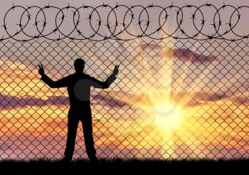 Concept of the refugees. Silhouette of a refugee in despair near the fence at sunset
