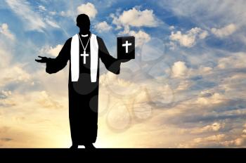concept of religion. Silhouette of a priest praying with the Bible in his hand against the evening sky in the sun