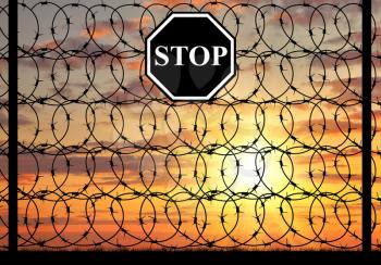 concept of refugee. Silhouette of fence with barbed wire and a stop sign at sunset