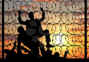 Concept of the refugees. Silhouette of illegally crossing the border refugees and stop sign on a fence with barbed wire