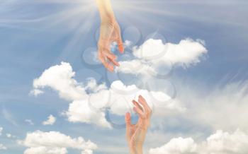  Concept of religion and God. Two hands reaching out to each other on the background of the cloudy sky