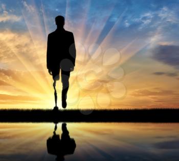 concept of rehabilitation of invalids with prosthetic legs. Walking disabled man at sunset and reflection in water