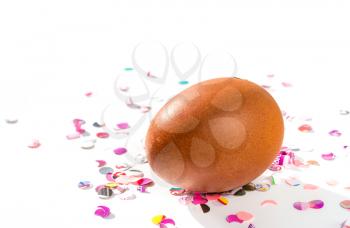 Brown chicken egg with shadow and colorful confetti on a white background.