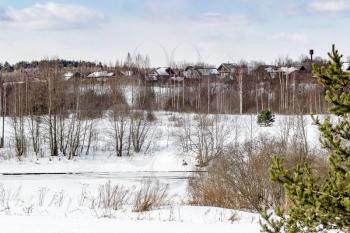 A beautiful March landscape with a village in the background and a frozen river.