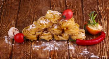 Pasta (tagliatelle) and flour on wooden surface.