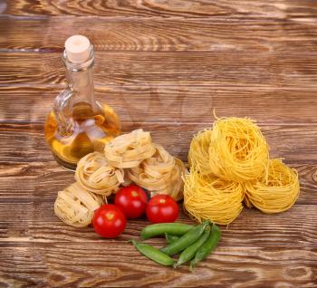 Pasta on the wooden background with tomato, lettuce pepper, olive oil and pepper