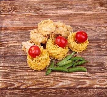 Pasta on the wooden background with tomato, pepper lettuce and pepper