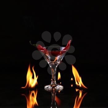 Red burning pepper in a glass with alcohol also burns with fire in black background