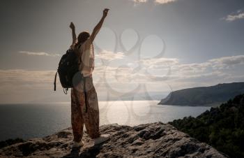 Hiker with backpack standing on top of a mountain with raised hands and enjoying view. Woman