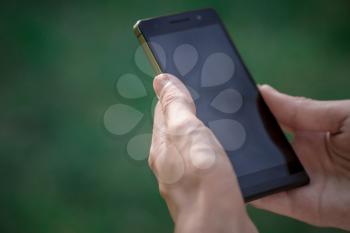 hand hold black smart phone, cell phone, mobile over blurred image of green forest background