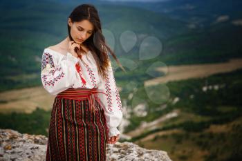 Attractive woman in traditional romanian costume on mountain green blurred background. Outdoor photo. Traditions and cultural diversity