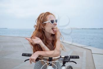 Beautiful woman riding on bike. Lifestyle and health in the city. Cheerful red-haired young woman gets pleasure from walking around the city