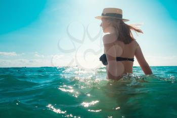 Beautiful woman having a fun while swimming in the sea. Beautiful romantic lady in a hat resting at sunset