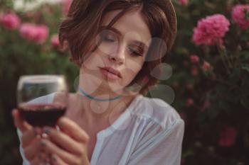 Beautiful young woman with curly hair posing near roses in a garden. The concept of perfume advertising