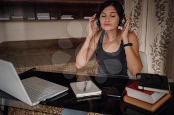 Young asian female student in headphones using laptop, communicates on internet. Cozy office workplace, remote work, E learning concept.