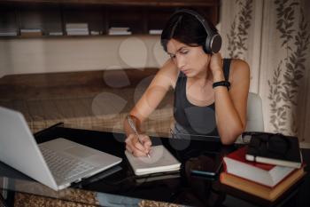 Young asian female student in headphones using laptop, writes notes . Cozy office workplace, remote work, E learning concept.