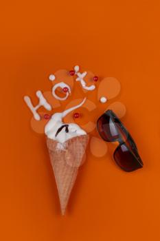 Ice cream cone filled with vanilla ice cream with sunglasses on an orange background. Summer concept. and the inscription Hot written by melted ice cream