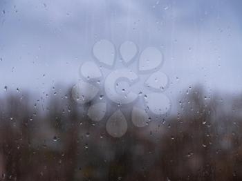 raindrops on window glass, autumn season. cityscape with trees in the background