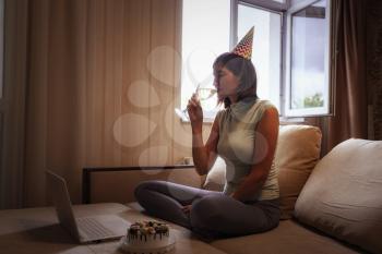 Girl celebrating birthday online in quarantine time. Woman celebrating her birthday through video call virtual party with friends. Authentic decorated home workplace. Coronavirus outbreak 2020.