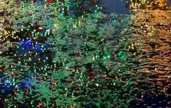 Reflection of the lights and branches of christmas trees in the part frozen surface of a pond or lake to give abstract xmas background