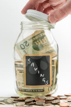 Hand opening lid of glass jar on white background with black chalk label and used for savings US dollar bills
