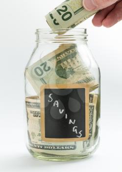 Caucasian hand putting money into glass jar on white background with black chalk label or panel and used for savings US dollar bills