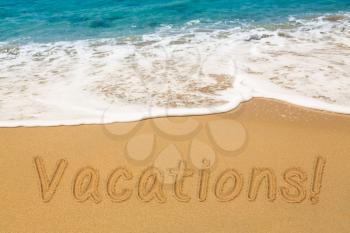 Vacations words written into sand on beach by warm blue ocean in Caribbean advertizing vacations and holidays