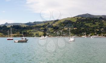 Yachts moored in Akaroa Harbor in New Zealand with the town and pier in the distance