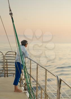 Middle aged caucasian woman on an ocean sunset cruise and leaning against the railings. Relaxed and looking at the horizon