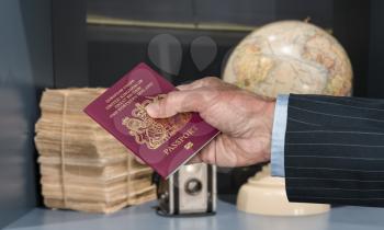 Senior executive hand holding UK passport against blurred background of world globe and camera