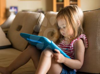 Young girl sitting at home on settee and using a child's tablet touch screen computer