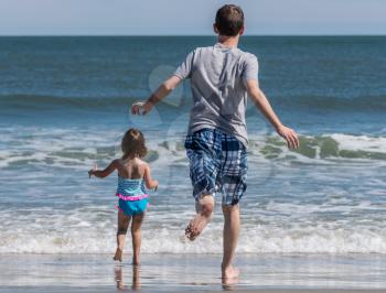 Back view of father and young girl running towards the sea in excitement