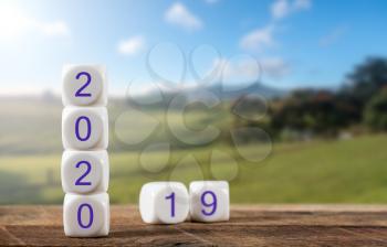 2020 spelled in cubes with 2019 behind on wooden table with sunlight on rural landscape