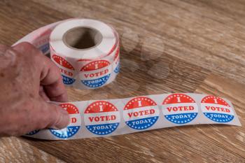 Large roll of I Voted Today stickers ready for voters in the US elections with senior mans hand