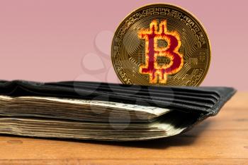 Bitcoin coin standing behind leather wallet stuffed with US dollar bills
