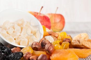 Pieces of dried pineapple, apricot, nuts and red apples on a wooden background. Various fruit snacks.
