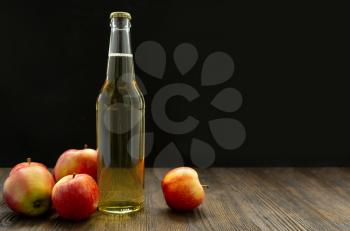 Hard apple cider in a glass bottle and red ripe apples on a black background